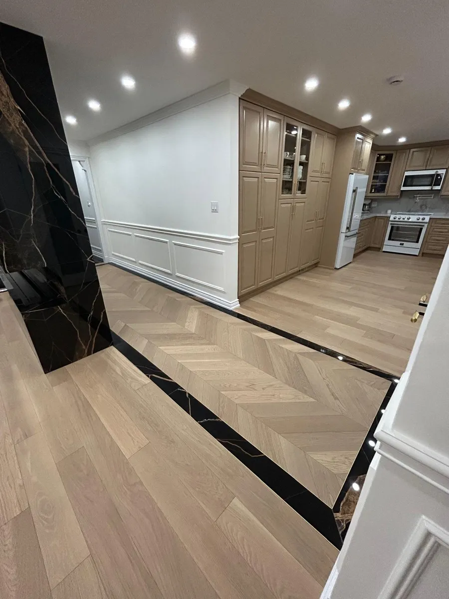 Light oak chevron flooring in a hallway leading to a kitchen, edged with a black marble border
