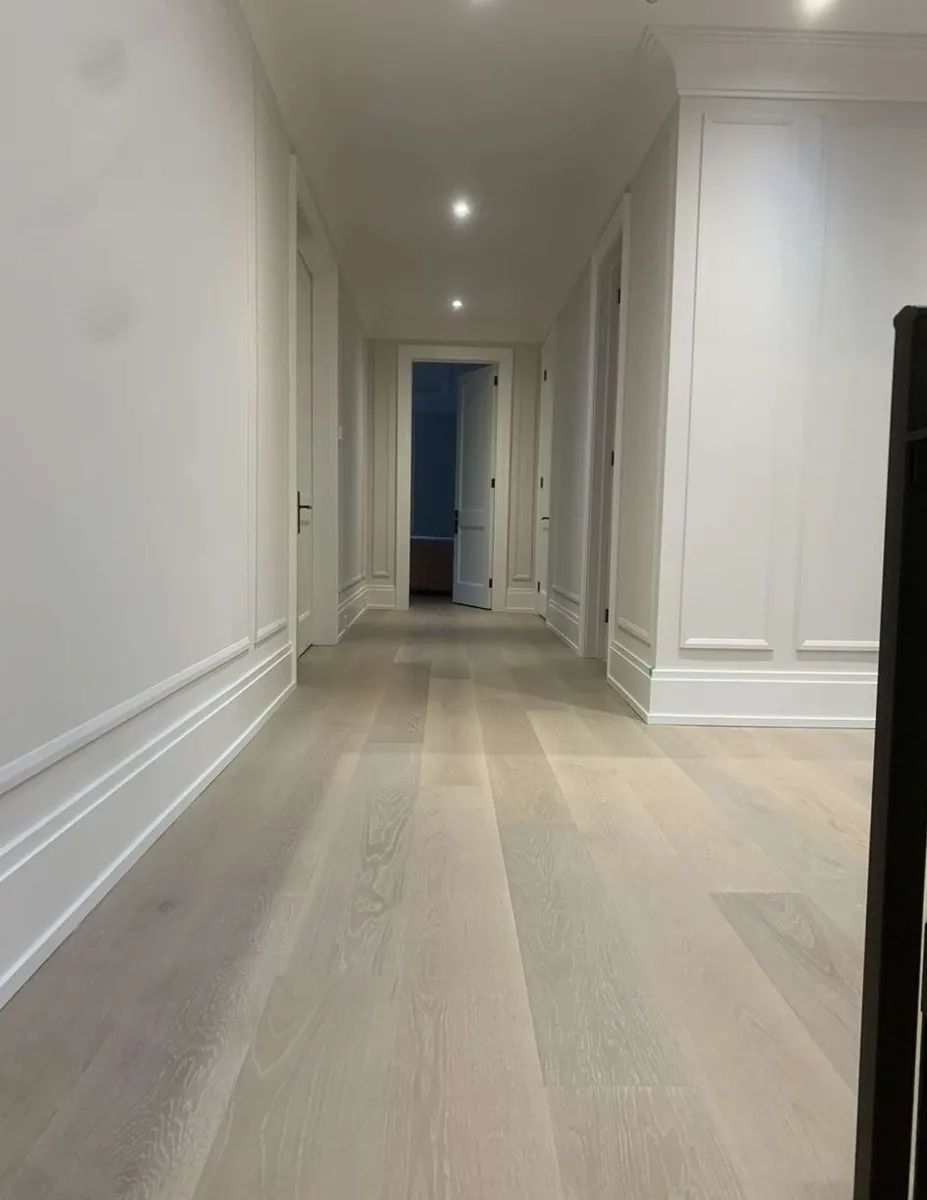 Light wide-plank engineered hardwood running the length of a long upstairs hallway with white wainscoting
