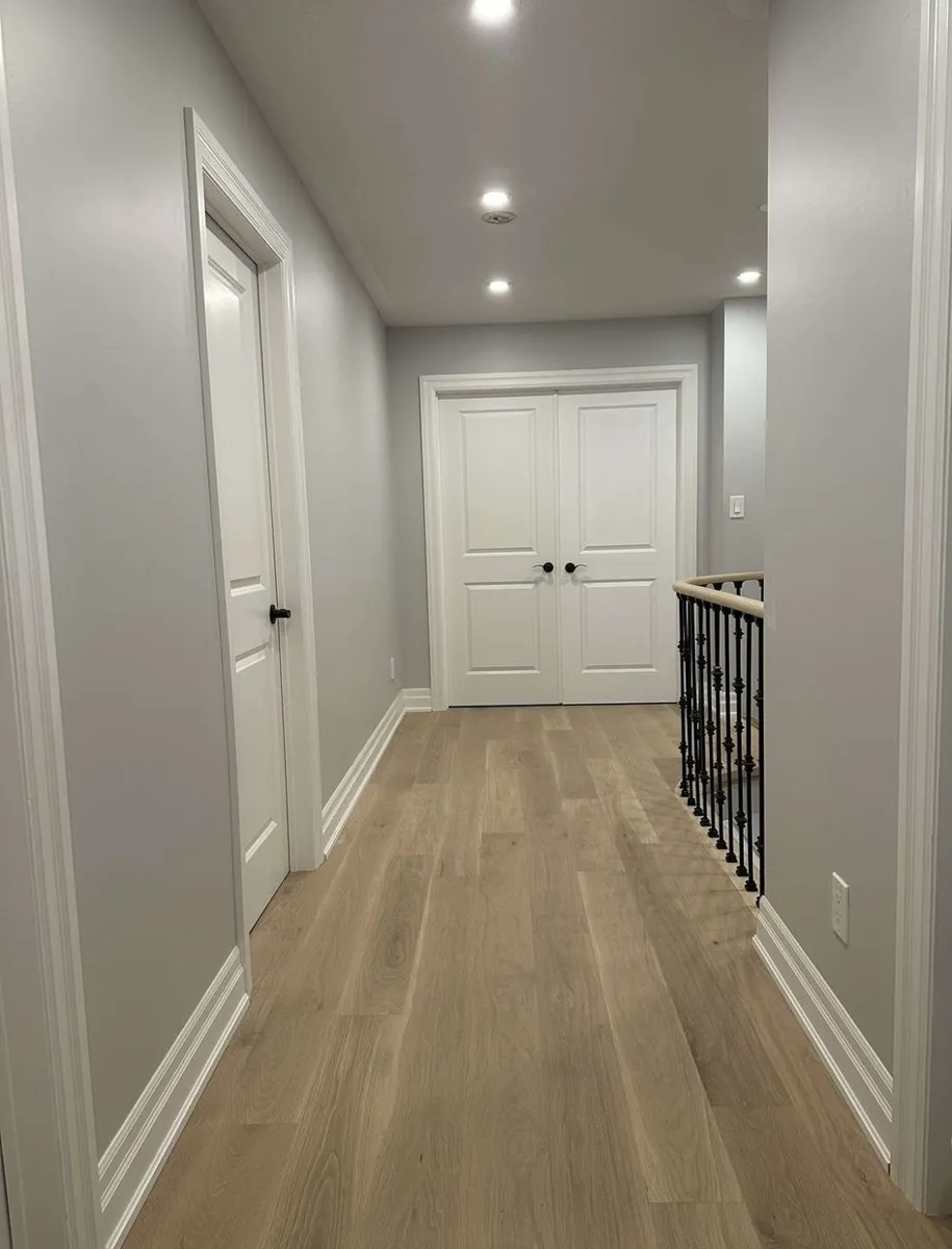 Light engineered hardwood laid through an upstairs hallway toward double doors, beside an iron stair railing