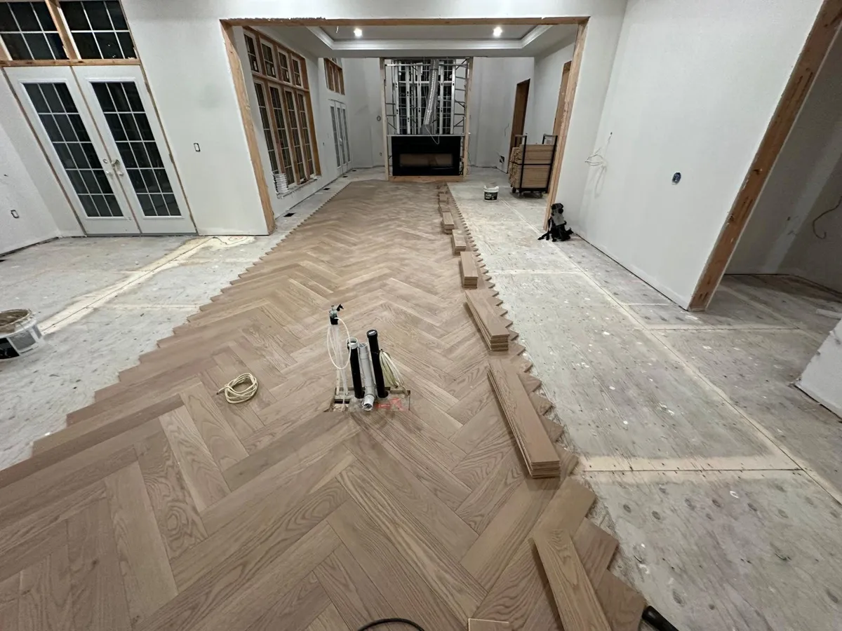 Light oak herringbone flooring partly laid across a large room, with installation tools on the floor