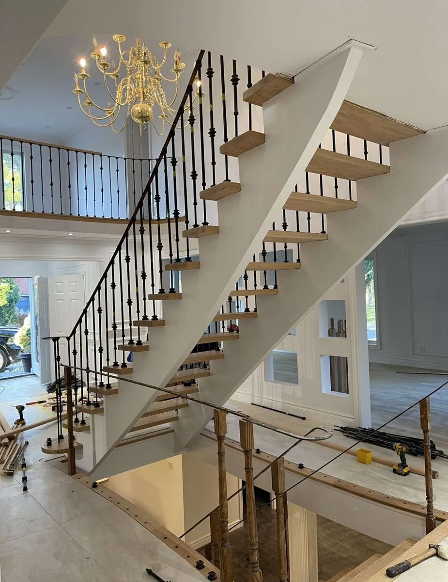 Open staircase with new wood treads and black iron pickets, still under construction in a two-storey foyer
