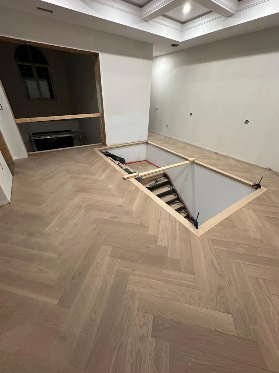 Stair opening framed into a light oak herringbone floor, with the stairs below