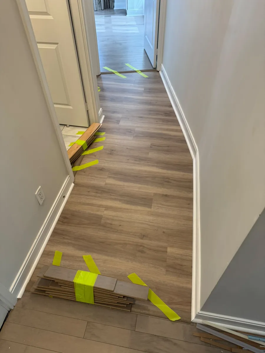 Plank flooring partly installed in a narrow hallway, with spare planks taped together on the floor